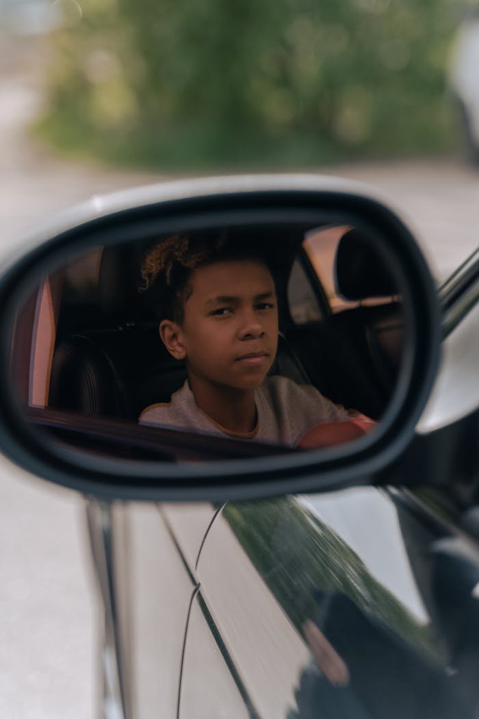 Teenager focused on driving, reflected in car's side mirror. A unique perspective on youth and responsibility.