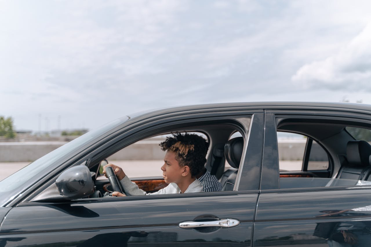 Side view of a young male teenager focused on driving a car in bright daylight.